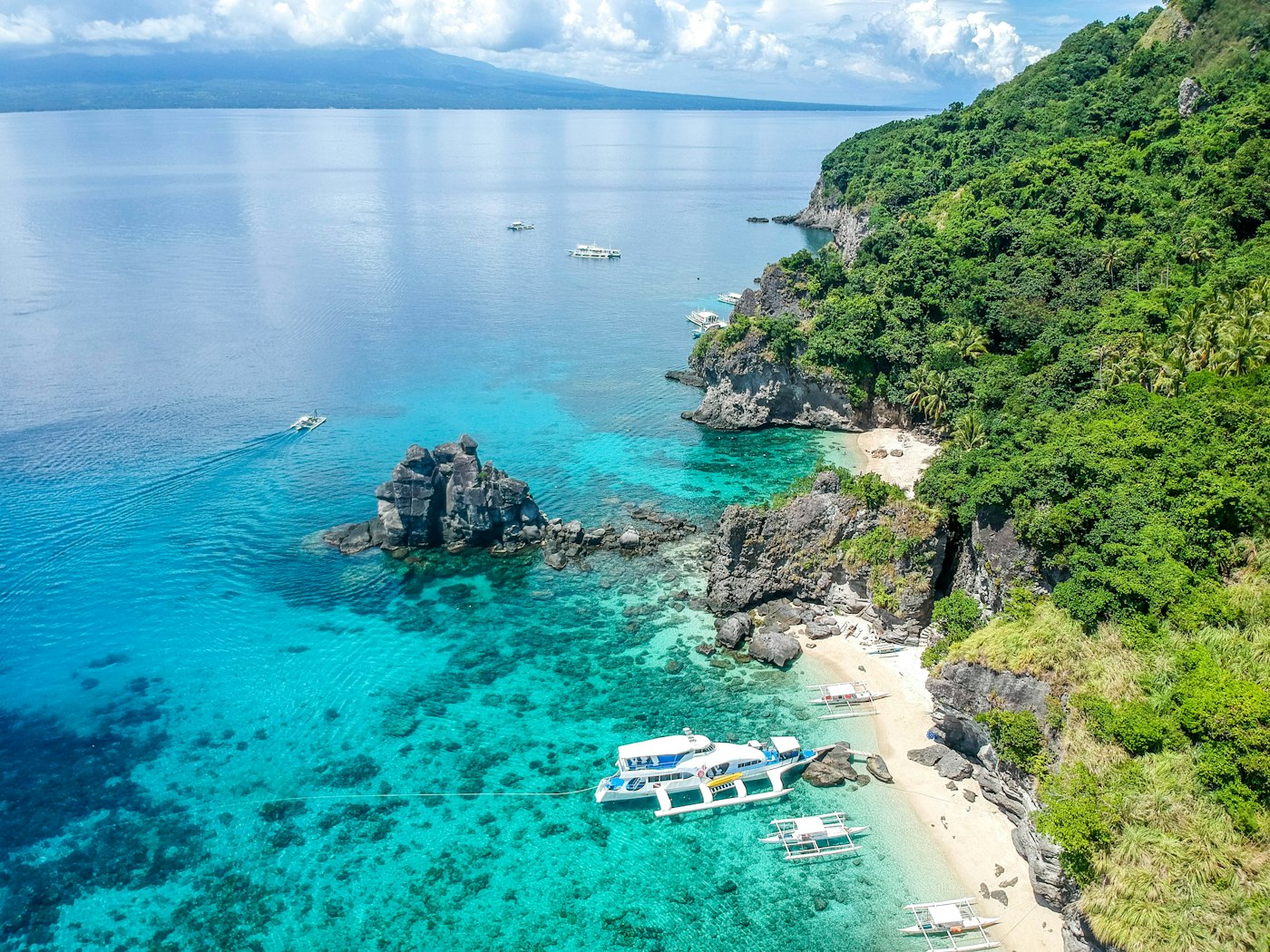 A turquoise Bohol cove with outrigger boats along a green shoreline